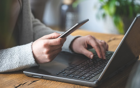 Person holding phone and on laptop