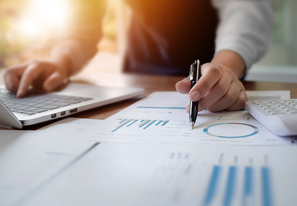 Person at a desk looking at charts and graphs in front of a laptop.